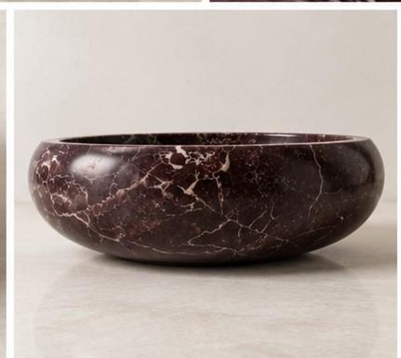 Pode incluir: Um lavat&oacute;rio redondo feito de m&aacute;rmore bord&ocirc; escuro com veios brancos proeminentes por toda a pedra. A bacia apresenta uma superf&iacute;cie exterior lisa e polida e uma forma de ta&ccedil;a profunda e larga concebida para instala&ccedil;&atilde;o em casas de banho.