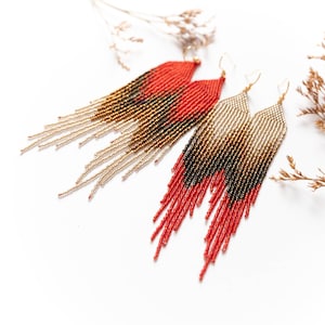 May include: A pair of long, beaded earrings with a gradient of red, gold, and black. The earrings are made with small, seed beads and have a fringe-like design.