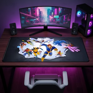 May include: A rectangular black desk mat featuring a colorful graphic illustration of a group of superhero characters in action poses. The characters are depicted in a central white burst design on the mat, which is placed on a wooden desk.