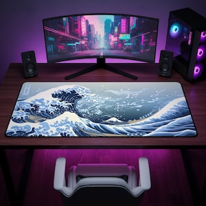 May include: A rectangular desk mat featuring a large-scale graphic print of a stylized ocean wave in shades of blue, white, and dark navy, with a small mountain peak visible in the background. The mat has a black border and a small white label.