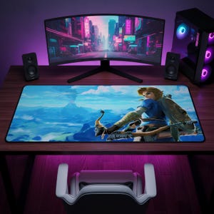 May include: A rectangular desk mat featuring a printed illustration of a blonde character holding a bow and arrow against a blue sky and mountain landscape. The mat has a black border and is positioned on a wooden desk in front of a computer monitor.