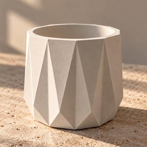 May include: A matte off-white planter with a geometric, faceted exterior design. The vessel features a wide circular opening at the top and a series of triangular, angular planes that create a structured, multi-sided silhouette around the body.