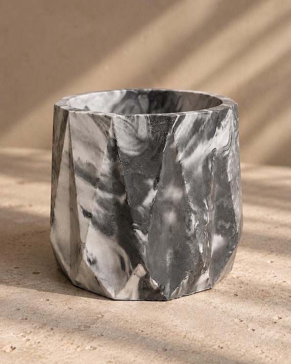 Sculptural faceted concrete planter with swirling black-and-white marble veining — looks like a gallery art object that also holds a plant.