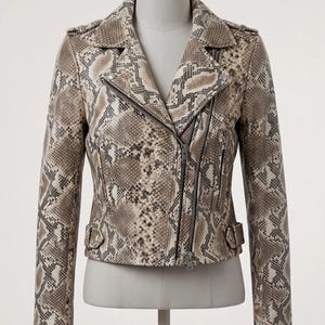 Könnte beinhalten: Eine Lederjacke mit beigem und braunem Schlangenledermuster, asymmetrischem Frontreißverschluss, Reverskragen, langen Ärmeln mit Reißverschlussbündchen und seitlichen Schnallenlaschen. Der Text AT Leathers ist oben links zu sehen.