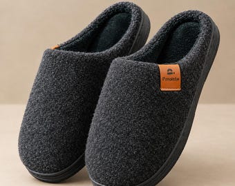 May include: A pair of dark gray slip-on slippers with a textured wool-like exterior and a black interior lining. Each slipper features a small tan rectangular tag on the side with the black text Pmoiste and a small icon above it.