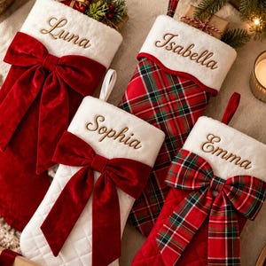 Könnte beinhalten: Vier Weihnachtsstrümpfe mit weißen Plüschbündchen, bestickt mit den Namen Luna, Isabella, Sophia und Emma. Zwei Strümpfe sind aus rotem Samt mit großen Schleifen, zwei weitere zeigen rot-grüne Karomuster mit passenden Schleifen.
