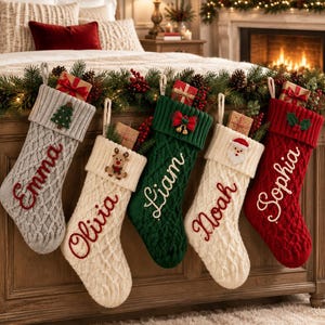 Può includere: Cinque calze natalizie in maglia a trecce appese in fila. Le calze sono grigie, color crema, verdi, color crema e rosse, ognuna con un nome ricamato in corsivo: Emma, Olivia, Liam, Noah e Sophia, decorate con icone natalizie.