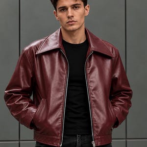Puede incluir: Una chaqueta de cuero color burdeos intenso con un cuello ancho en punta, una cremallera frontal plateada de longitud completa y dos bolsillos laterales. La chaqueta se lleva sobre una camiseta negra lisa y vaqueros oscuros, con acabado liso.