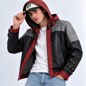 Puede incluir: Una chaqueta con capucha que presenta un diseño de bloques de color en rojo, negro y gris. La chaqueta incluye una capucha roja, paneles principales negros, detalles grises en los hombros y correas con hebilla ajustables en los puños.