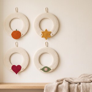May include: Four circular wall hangings made of off-white coiled rope, each featuring a small crocheted accent at the bottom. The accents include an orange pumpkin, a yellow six-pointed star, a dark pink heart, and a green and pink eye shape.