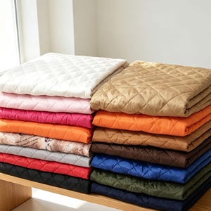 Peut inclure: Une pile de carrés de tissu matelassé pliés dans diverses couleurs, notamment blanc, rose, magenta, orange, beige, marron, bleu, vert et noir, avec un carré présentant un motif imprimé de texte et d'illustrations sur fond clair.