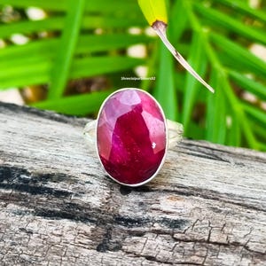 May include: A silver ring featuring a large, oval-shaped, faceted deep pink gemstone set in a smooth metal bezel. The ring band is split into two thin silver segments. The text ShreeJaipurSilvers92 is visible above the ring.