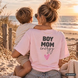 Può includere: Una t-shirt a maniche corte rosa chiaro con la scritta nera BOY MOM energy stampata sul retro, accompagnata da un piccolo cuore rosa sotto il testo. La maglietta è indossata con jeans blu ed è mostrata vista dal retro.
