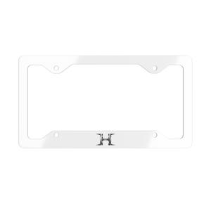 Peut inclure: Un cadre de plaque d'immatriculation rectangulaire blanc aux coins arrondis avec quatre trous de montage. Le cadre présente une lettre H en argent métallique centrée sur le bord inférieur, conçue avec une police stylisée et une finition brillante.