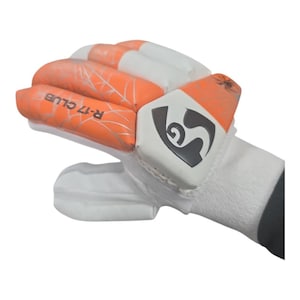May include: A white and orange cricket batting glove featuring padded finger sections with a spiderweb pattern. The text R-17 CLUB is printed on the orange section, and a black SG logo is displayed on the white wrist and thumb protection area.