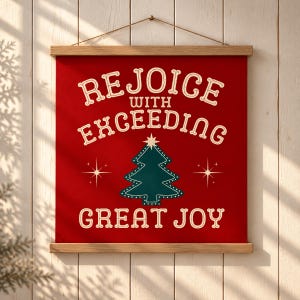 May include: A red fabric wall hanging with wooden top and bottom rails, featuring the cream-colored text REJOICE WITH EXCEEDING GREAT JOY and a dark green Christmas tree graphic with a star, suspended by a thin brown string.