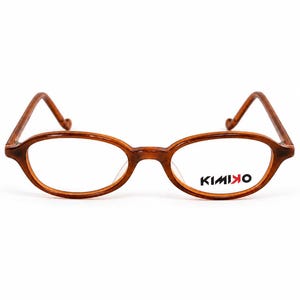 以下が含まれることがあります： 茶色のべっ甲柄フレームの楕円形メガネ。右レンズの表面には黒と赤でKIMINOという文字がプリントされています。メガネには細いテンプルと、2つの楕円形のリムをつなぐブリッジが付いています。