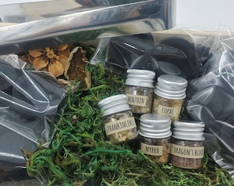 May include: A wooden box filled with green moss and small glass jars containing various resins, including frankincense, myrrh, benzoin, copal, and dragon's blood. The box also contains black charcoal discs and a metal tongs.