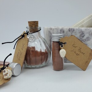 May include: Three glass jars with brown powder and labels. The labels say "Star Anise", "Red Rice Dust", and "Ground Nutmeg". The jars are on a white surface with a marble mortar and pestle.