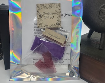 May include: A Fearlessness Spell Kit in a clear plastic bag with a purple fabric, a red ribbon, a small white stone, and a small brown paper tag that says "dragon's blood".