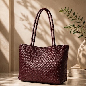 Può includere: Una borsa tote color bordeaux intenso caratterizzata da un intricato motivo intrecciato su tutto l'esterno. La borsa include due lunghi manici intrecciati fissati al bordo superiore, offrendo una consistenza uniforme al design.