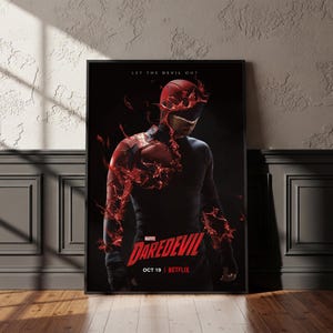 Op de afbeelding: Een ingelijste poster met het Marvel-personage Daredevil in een donker pak met een rood masker, omringd door wervelende rode vloeistofeffecten. De tekst luidt LET THE DEVIL OUT, MARVEL DAREDEVIL, OCT 19 en NETFLIX tegen een zwarte achtergrond.