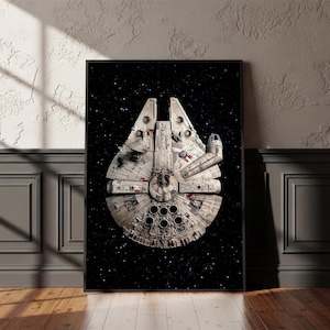 Op de afbeelding: Een ingelijste rechthoekige wandkunstprint met het Millennium Falcon ruimteschip gecentreerd tegen een donkere zwarte achtergrond vol verspreide witte sterren. Het ruimteschip is gedetailleerd in off-white, grijs en rode accenten.