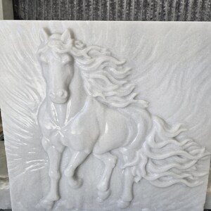 May include: A square white marble wall plaque featuring a high-relief carving of a horse in motion. The horse is depicted with a flowing mane and tail, with subtle carved lines in the background suggesting movement or wind across the stone surface.
