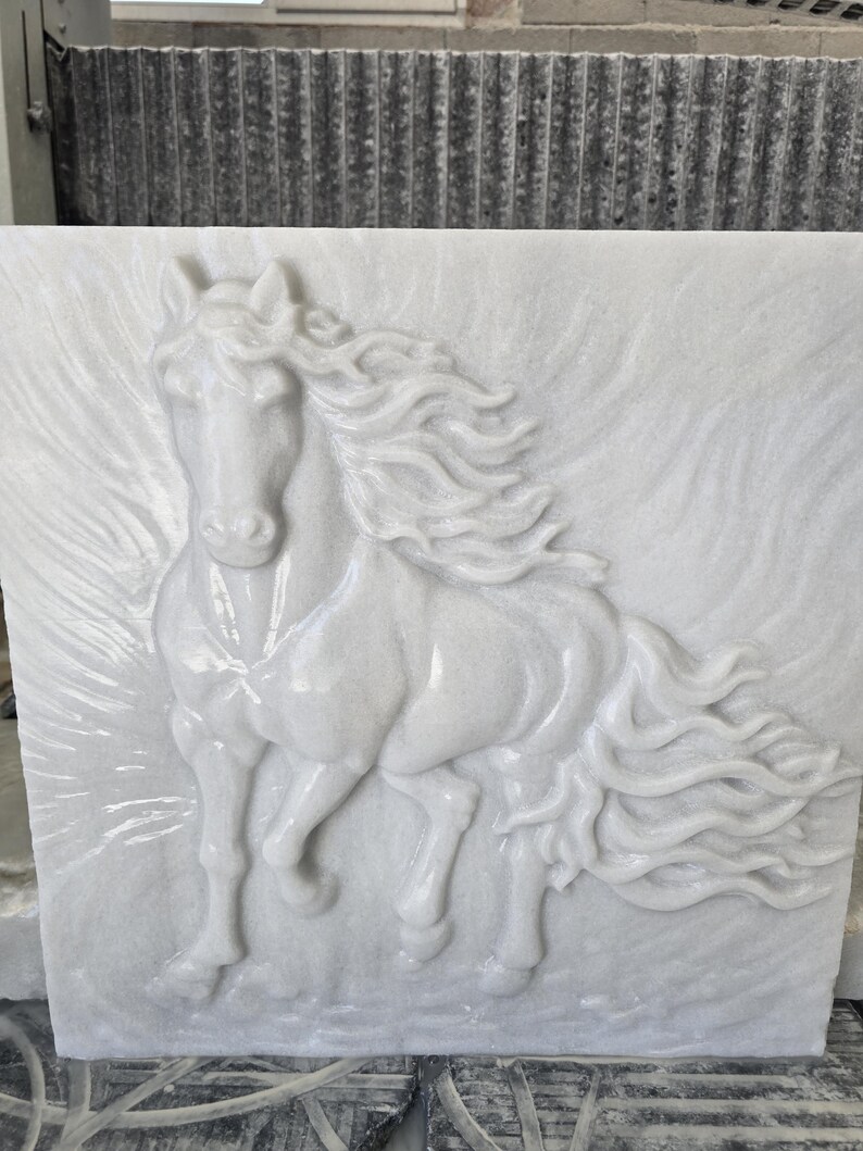 May include: A square white marble wall plaque featuring a high-relief carving of a horse in motion. The horse is depicted with a flowing mane and tail, with subtle carved lines in the background suggesting movement or wind across the stone surface.