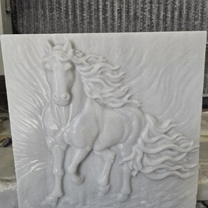 May include: A square white stone tile featuring a high-relief carving of a horse in motion. The horse is depicted facing forward with a flowing mane and tail that extend across the surface, creating a dynamic sense of movement in the stone.