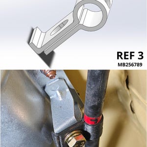 May include: A gray metal mounting bracket with a circular opening and an elongated slot, labeled REF 3 MB256789. The bracket is shown in a technical diagram and installed on a vehicle component, securing a black pipe with a bolt and a red marker.