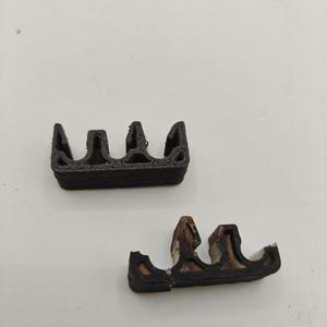 May include: Two small, black, 3D-printed plastic components with a multi-channel, wavy profile. The top piece is solid black with a layered texture, while the bottom piece shows signs of wear with white material visible along the edges.
