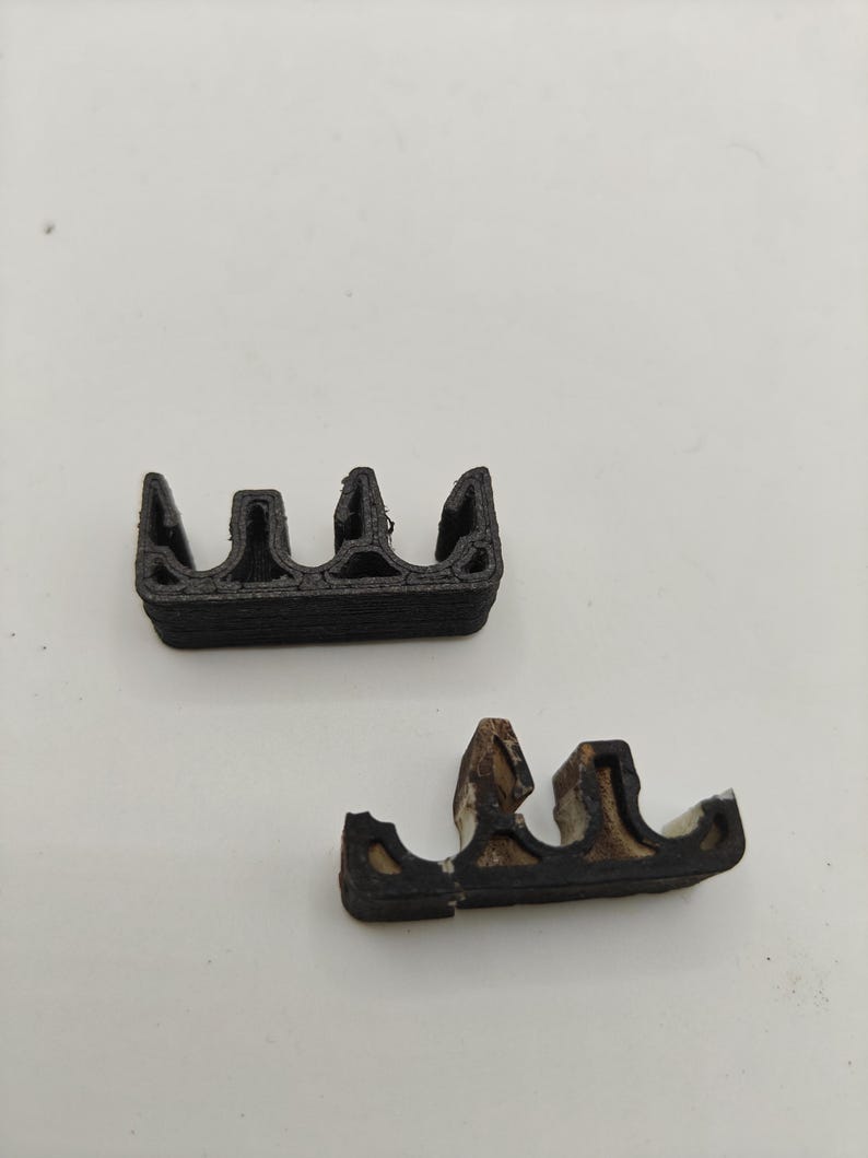May include: Two small, black, 3D-printed plastic components with a multi-channel, wavy profile. The top piece is solid black with a layered texture, while the bottom piece shows signs of wear with white material visible along the edges.