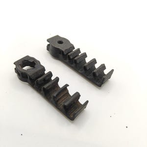 May include: Two black, 3D-printed plastic cable management clips. Each piece features a circular mounting hole at one end and a series of four open-ended, C-shaped channels designed to hold and organize individual wires or cables in a row.