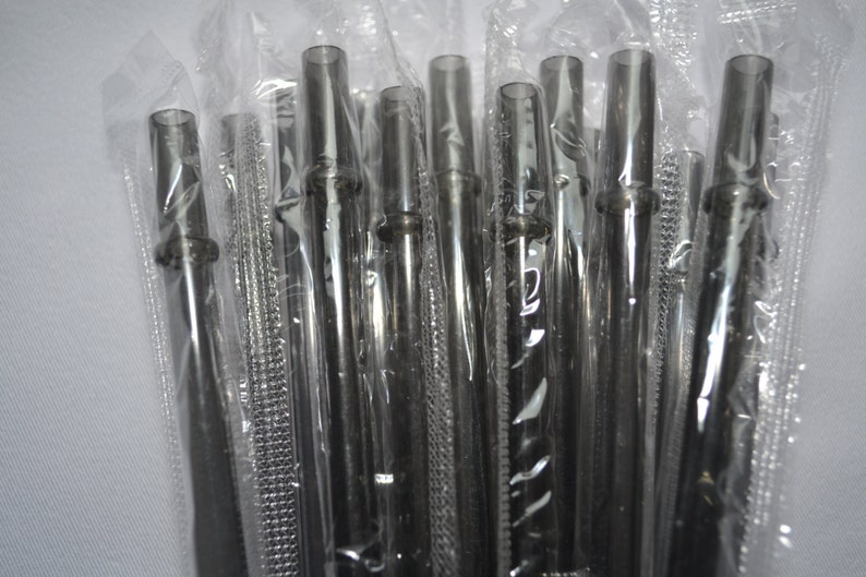 May include: A collection of black reusable straws, each encased in transparent plastic. The straws are cylindrical, featuring a subtle flare at the top and a small ring near the base. The image is a close-up, emphasizing the texture and design of the straws.