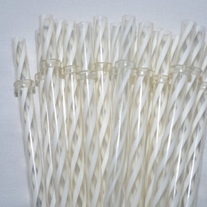 May include: A bundle of clear, transparent glass straws with a white, spiral design. The straws are held together by a clear plastic ring. The straws are approximately 8 inches long.