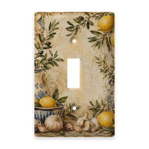 May include: A rectangular light switch cover plate featuring a printed still life illustration of yellow lemons, green olive branches, garlic bulbs, and blue and white patterned ceramic pottery against a distressed beige background.