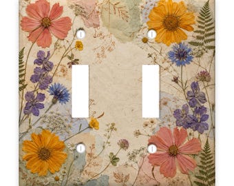 May include: A double light switch cover plate featuring a collage of pressed dried flowers including pink cosmos, yellow daisies, blue cornflowers, and green ferns on a textured cream-coloured paper background with four screw holes.