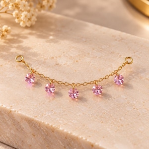May include: A gold-toned chain connector featuring five round, faceted pink crystals suspended at regular intervals. The delicate metal chain has a small circular jump ring at each end, designed for attachment to jewelry pieces.