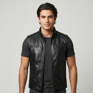 Può includere: Un gilet in pelle nera con colletto alla coreana, chiusura frontale con zip, due tasche sul petto con zip e due tasche inferiori con zip. Il gilet presenta dettagli trapuntati sulle spalle ed è indossato sopra una t-shirt grigio scuro.