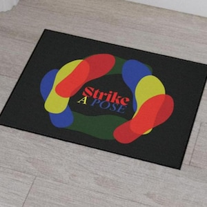 May include: Black doormat with a colorful design of overlapping circles in red, yellow, blue, and green. The text "Strike A Pose" is printed in white on the doormat.