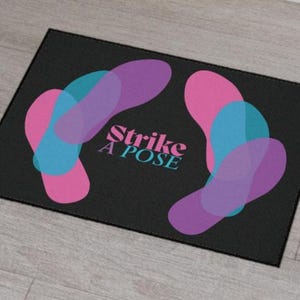 May include: Black doormat with the text "Strike a Pose" in white and pink. The doormat features a design of overlapping pink, purple, and blue shapes.