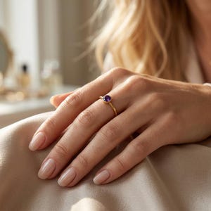 Puede incluir: Un anillo fino de oro con una piedra preciosa morada redonda engastada en bisel. La banda es lisa y pulida, mostrando un diseño sencillo que resalta el tono violeta intenso de la piedra central, la cual está sujeta en un engaste de oro.
