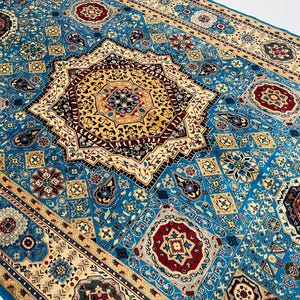 May include: A rectangular area rug featuring a vibrant blue background with a large central star-shaped medallion in gold, black, and red. The surface is covered in intricate geometric patterns, floral motifs, and repeating octagonal shapes.