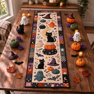 May include: A rectangular fabric table runner featuring a patchwork border and a central panel decorated with illustrations of black cats, ghosts, pumpkins, witch hats, and bats. The runner is displayed on a wooden table with pumpkins.