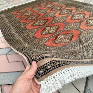 May include: A rectangular area rug featuring a repeating geometric pattern of orange octagons and dark brown borders. The rug has a dense, intricate design with small floral motifs inside each shape and a white fringe along the short edge.