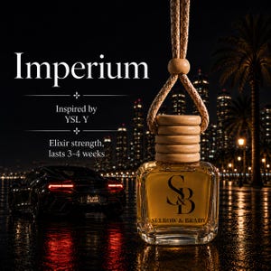 May include: A square glass car air freshener bottle with a light brown wooden cap and a hanging rope. The bottle features the black text 'S&B' and 'SELROW & BRADY'. The background displays the text 'Imperium', 'Inspired by YSL Y', and 'Elixir strength, lasts 3-4 weeks'.