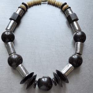 Puede incluir: Un collar negro y plateado con cuentas redondas y en forma de disco. El collar tiene un diseño geométrico.