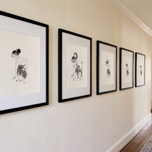 Könnte beinhalten: Eine Serie von fünf gerahmten Wandbildern mit schwarzen Tuschezeichnungen stilisierter Figuren auf cremefarbenem Papier. Jedes Bild ist in einem schlichten schwarzen Rahmen mit weißem Passepartout gefasst und horizontal an einer Wand angeordnet.