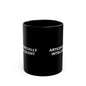 May include: A black cylindrical mug featuring the white text ARTIFICIALLY INTELLIGENT printed on the side. The mug has a smooth, glossy finish and a standard handle-less design, displaying the text clearly against the dark background.